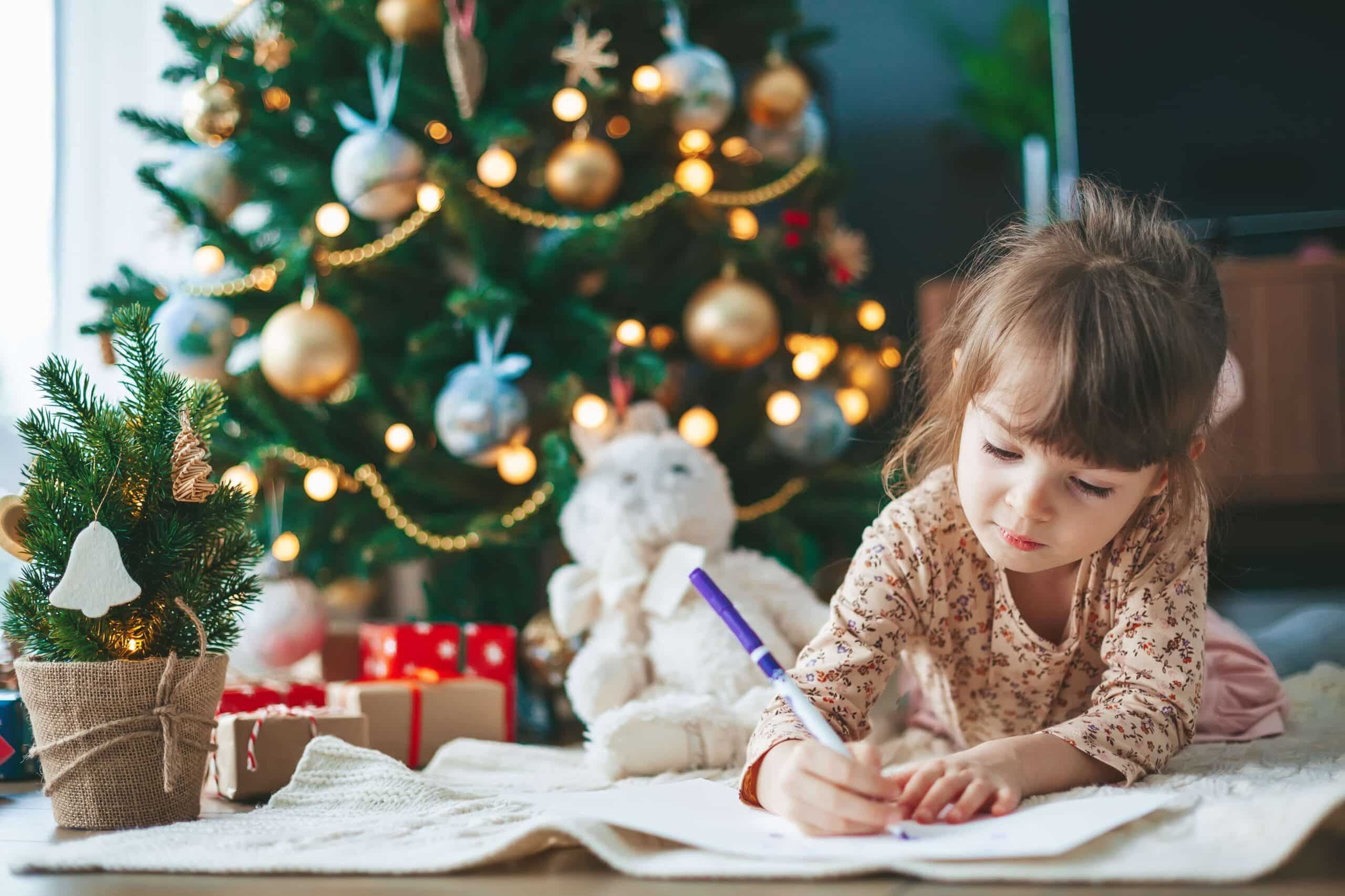 little child girl writing letter near Christmas tree. Symbolic of topic about christmas arrangements for separated parents.