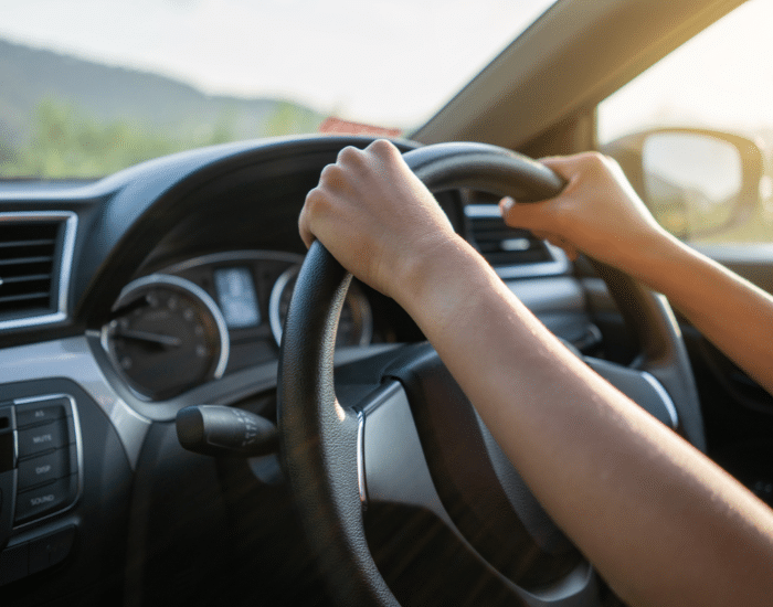 Person's hands on the steering wheel of a vehicle with trees and mountains in the background. Symbolic of this page's topic: Drug Driving Lawyers